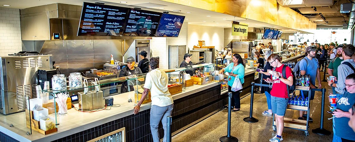 People are ordering food at a busy fast-food restaurant counter.